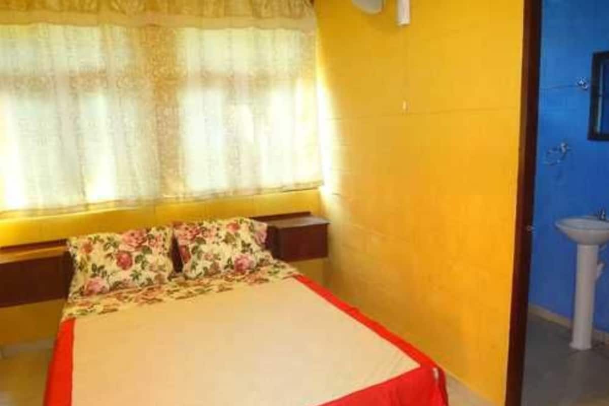 A bedroom with a bed, a window with curtains, and a bathroom with a sink.