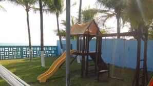 Ein Spielplatz mit Rutsche und Klettergerüst, umgeben von einem blauen Zaun und Palmen.