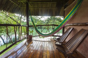 Terraza de madera con hamaca y bancos con vista a un cuerpo de agua.