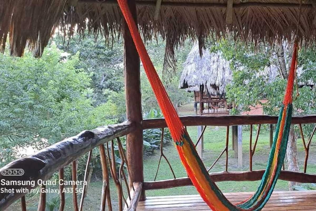 A wooden deck with a hammock, a thatched roof, and a view of a lush garden.