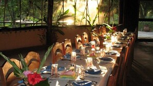 A dining table set for a meal with chairs, candles, and a view of the outdoors. - Cotton Tree Lodge (Punta Gorda)
