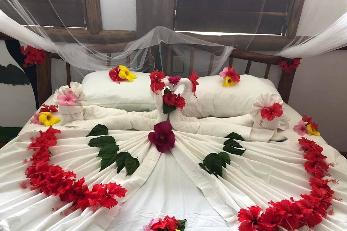 A bed with white linens, red and yellow flowers, and a canopy.