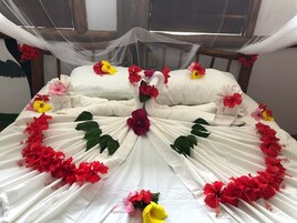 Una cama con sábanas blancas, flores rojas y amarillas, y un dosel.