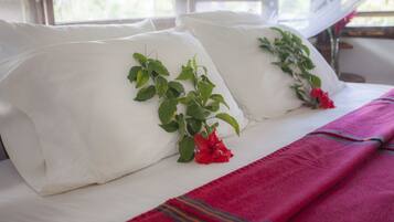 Uma cama com almofadas brancas, um cobertor vermelho e folhas verdes com flores vermelhas sobre as almofadas.