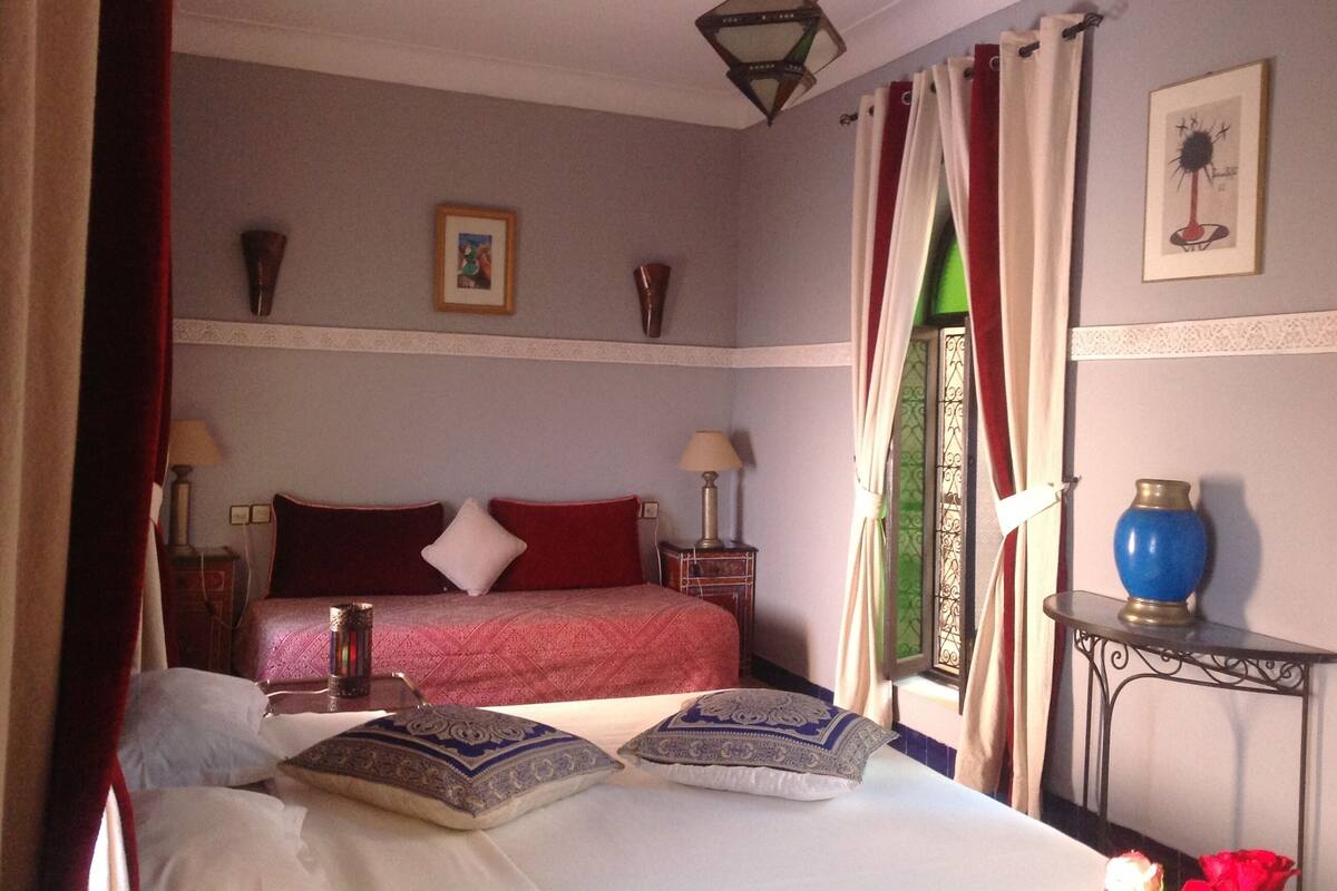 A bedroom with a bed, two bedside tables, a nightstand, a lamp, a vase, and a picture on the wall.
