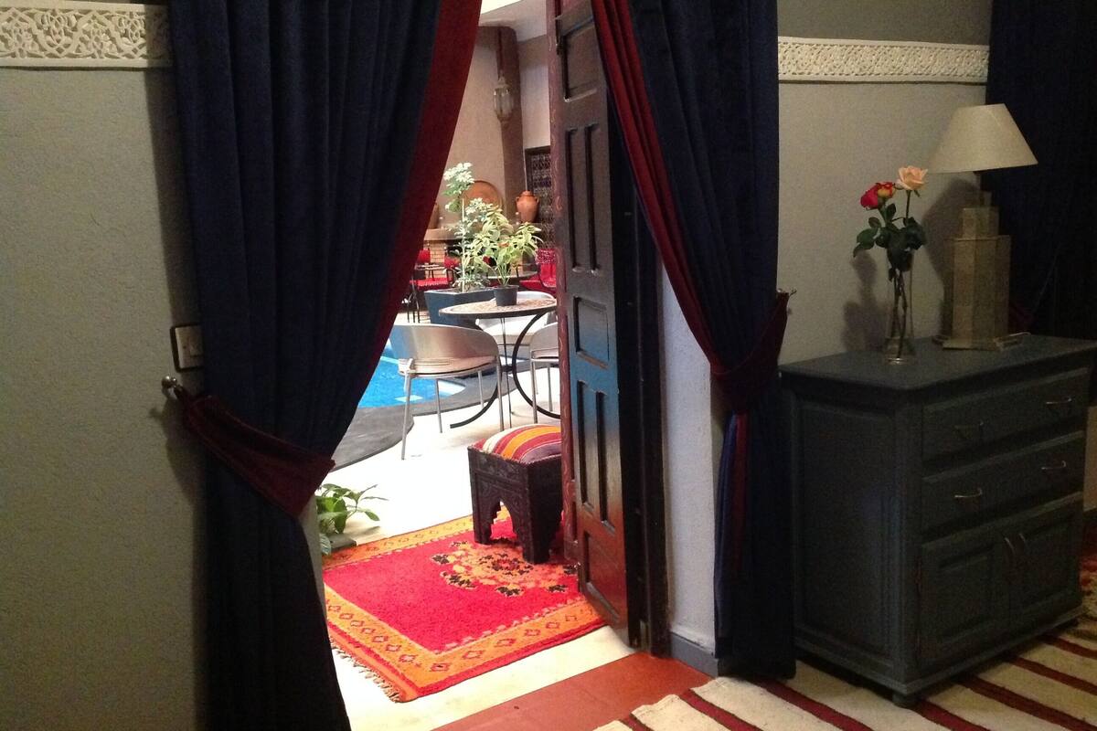 A doorway leading to a dining area with a red and yellow patterned rug, a table with chairs, and a potted plant.