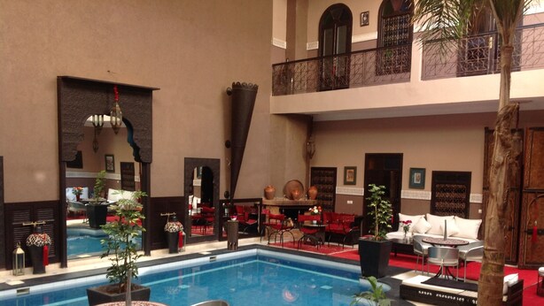 Una piscina interior con sillones y mesas, rodeada de sillas rojas y plantas en macetas.