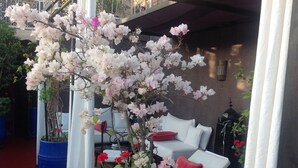 Un patio con asientos blancos acolchados, un árbol en maceta con flores y una maceta azul.