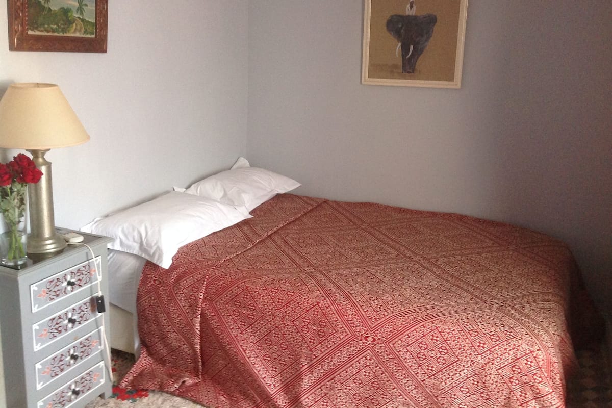 A bedroom with a bed, a nightstand with a lamp and flowers, and two framed pictures on the wall.