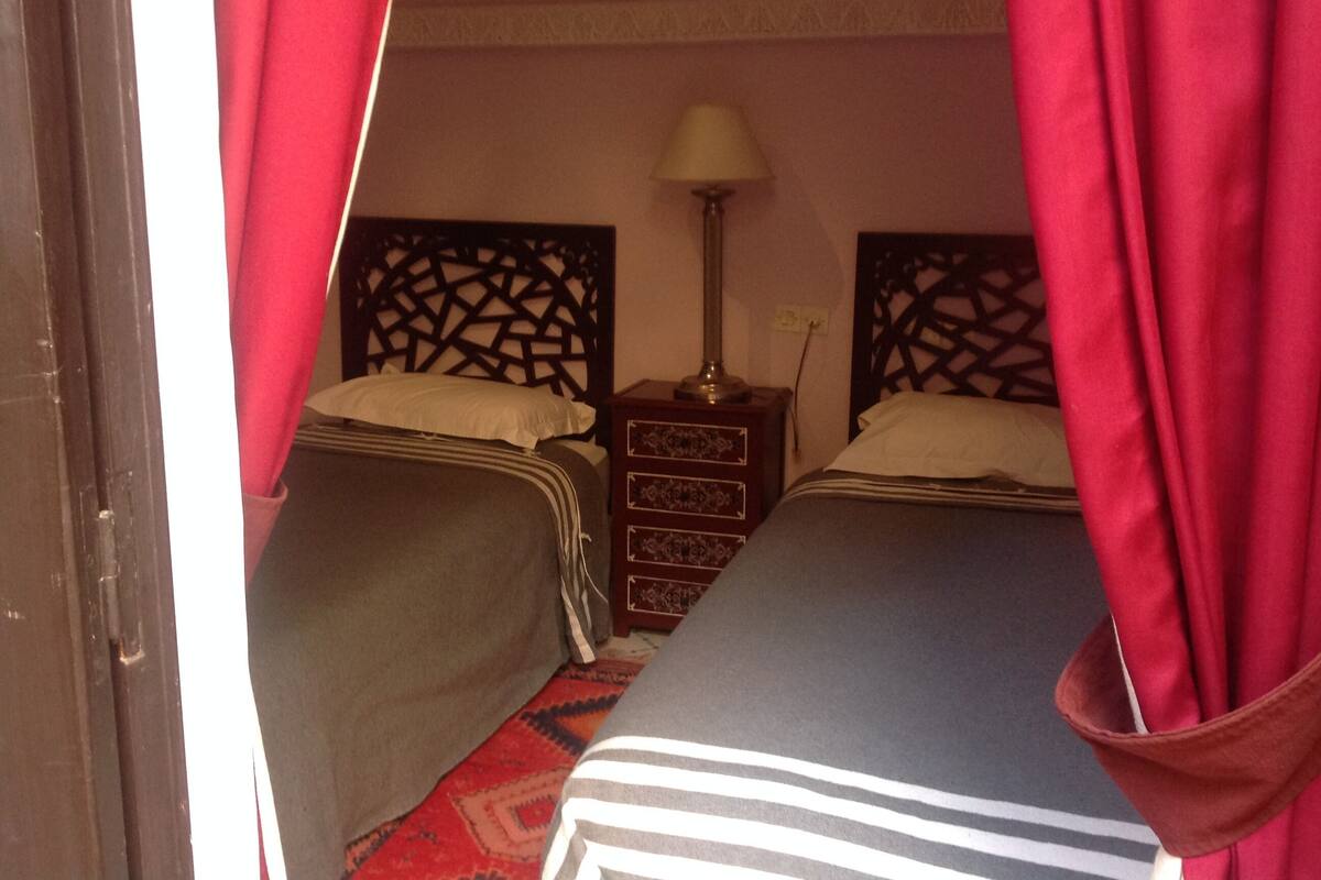 A hotel room with two beds, a nightstand, a lamp, and a patterned rug.