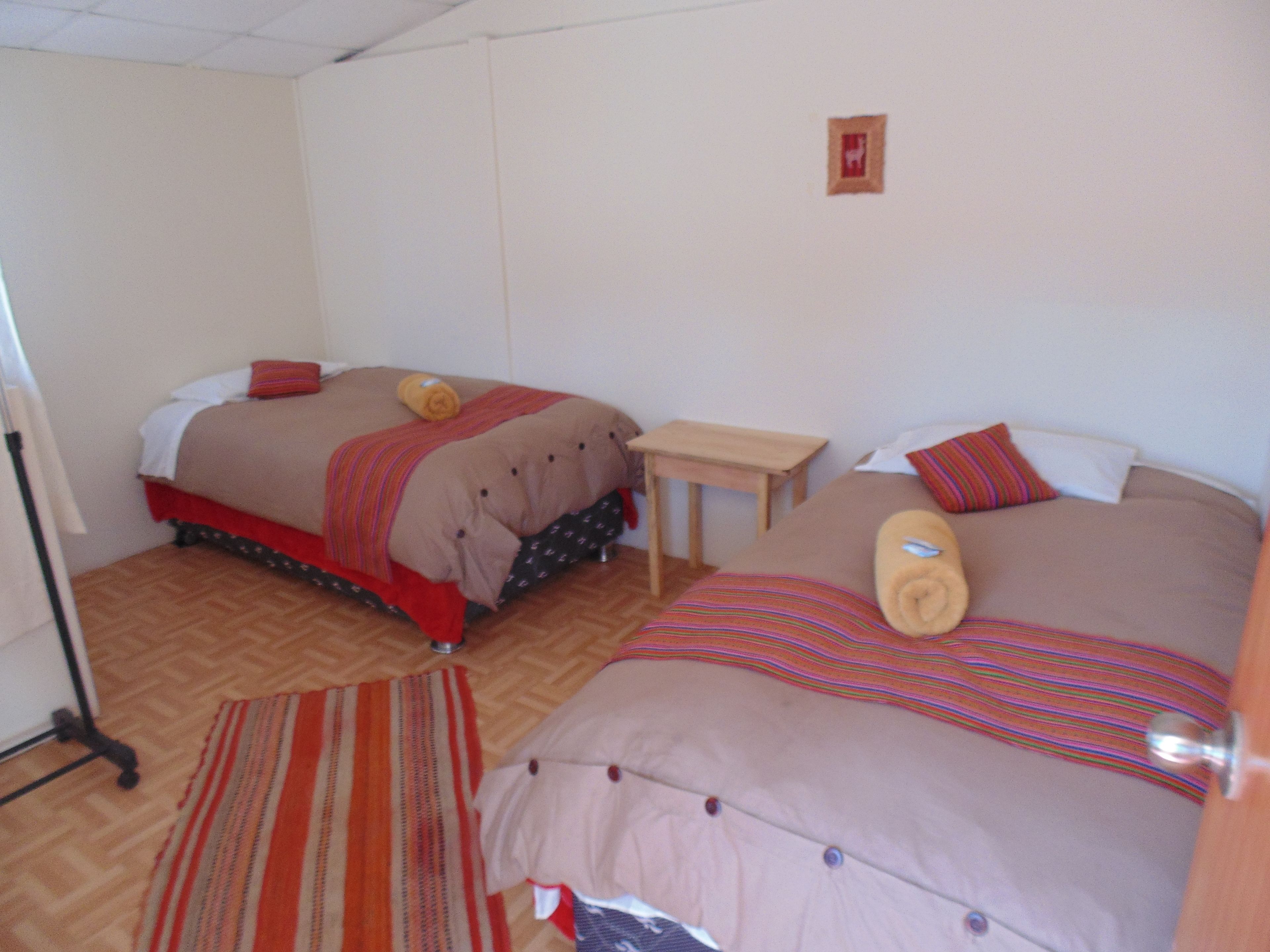 A hotel room with two beds, a small table, and a striped rug.