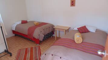 A hotel room with two beds, a small table, and a striped rug.