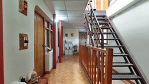 A hallway with a wooden floor, a staircase with colorful decorations, and a desk with a computer and figurines. - Magic Cusco (Cusco)