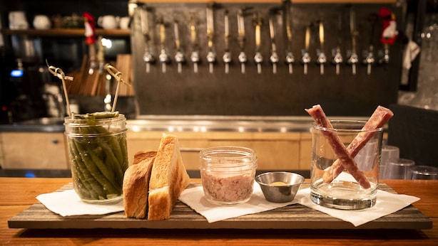 A wooden table with a jar of pickles, two slices of bread, a small bowl of mustard, and a glass with bacon. - Auberge Sutton Brouerie (Sutton)