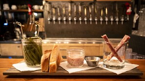 A wooden table with a jar of pickles, two slices of bread, a small bowl of mustard, and a glass with bacon. - Auberge Sutton Brouerie (Sutton)