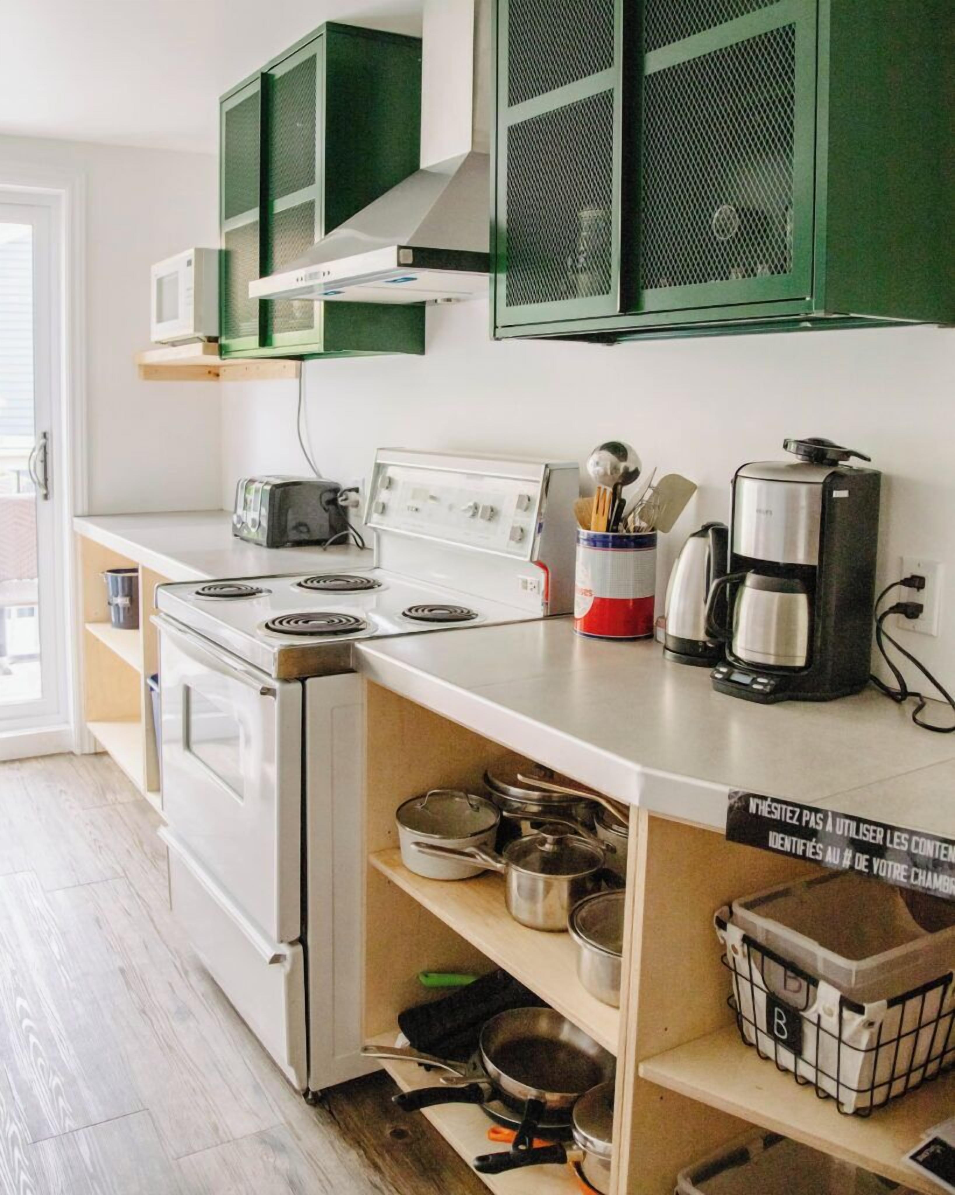A kitchen with white appliances, green cabinets, and a coffee maker.