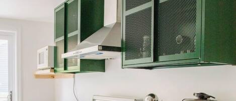 A kitchen with white appliances, green cabinets, and a coffee maker.