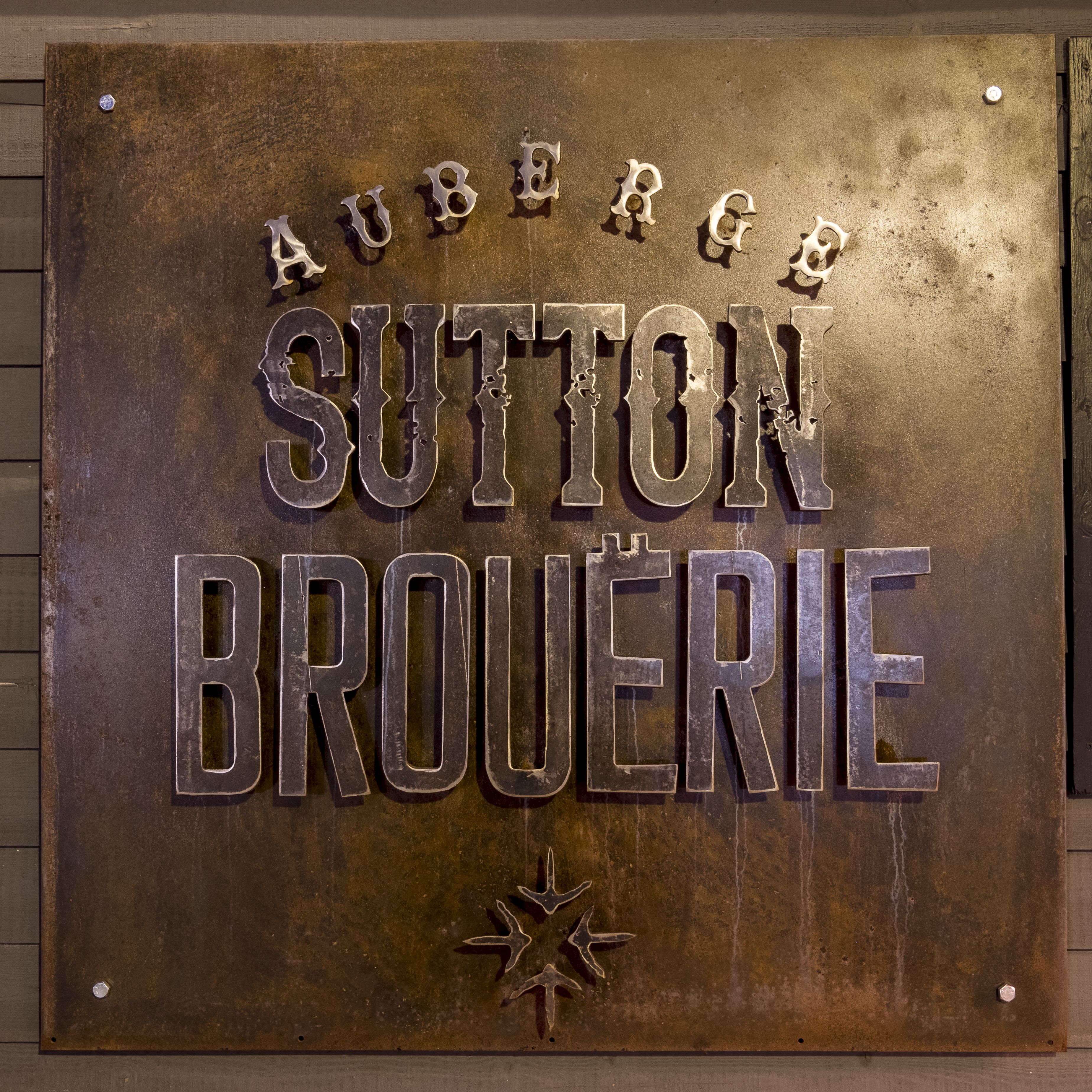 Un letrero de metal con el texto "AUBERGE SUTTON BROUÉRIE" y un símbolo de estrella debajo del texto.