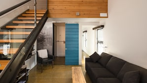 A modern interior with a staircase, a blue door, a dark sofa, and a wooden coffee table. - Auberge Sutton Brouerie (Sutton)