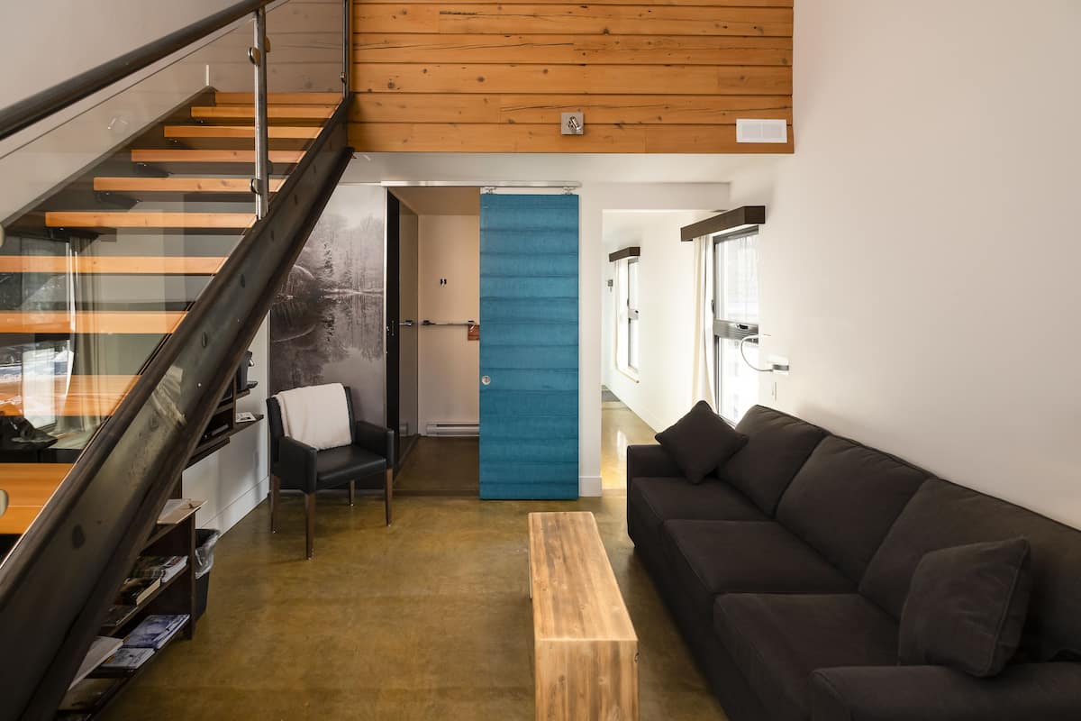 A modern interior with a staircase, a blue door, a dark sofa, and a wooden coffee table.