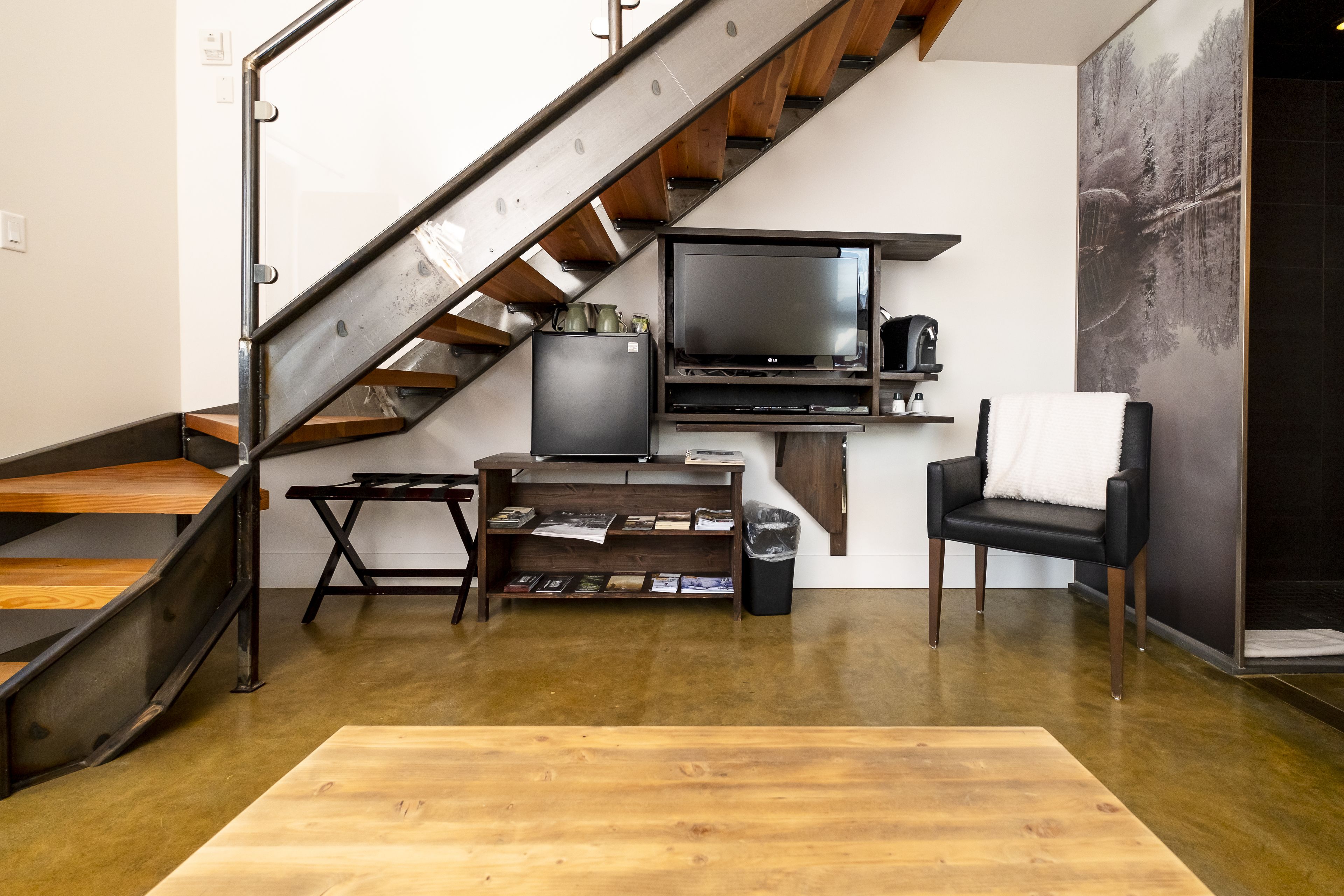 A modern living room with a wooden staircase, a flat-screen TV, a bookshelf, and a black leather chair.