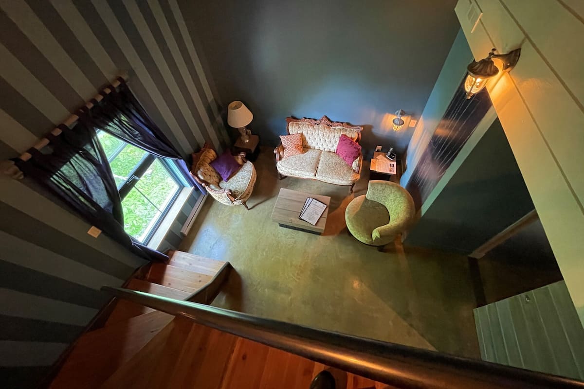 A room with a sofa, a chair, a table, and a lamp. There is a window with curtains.