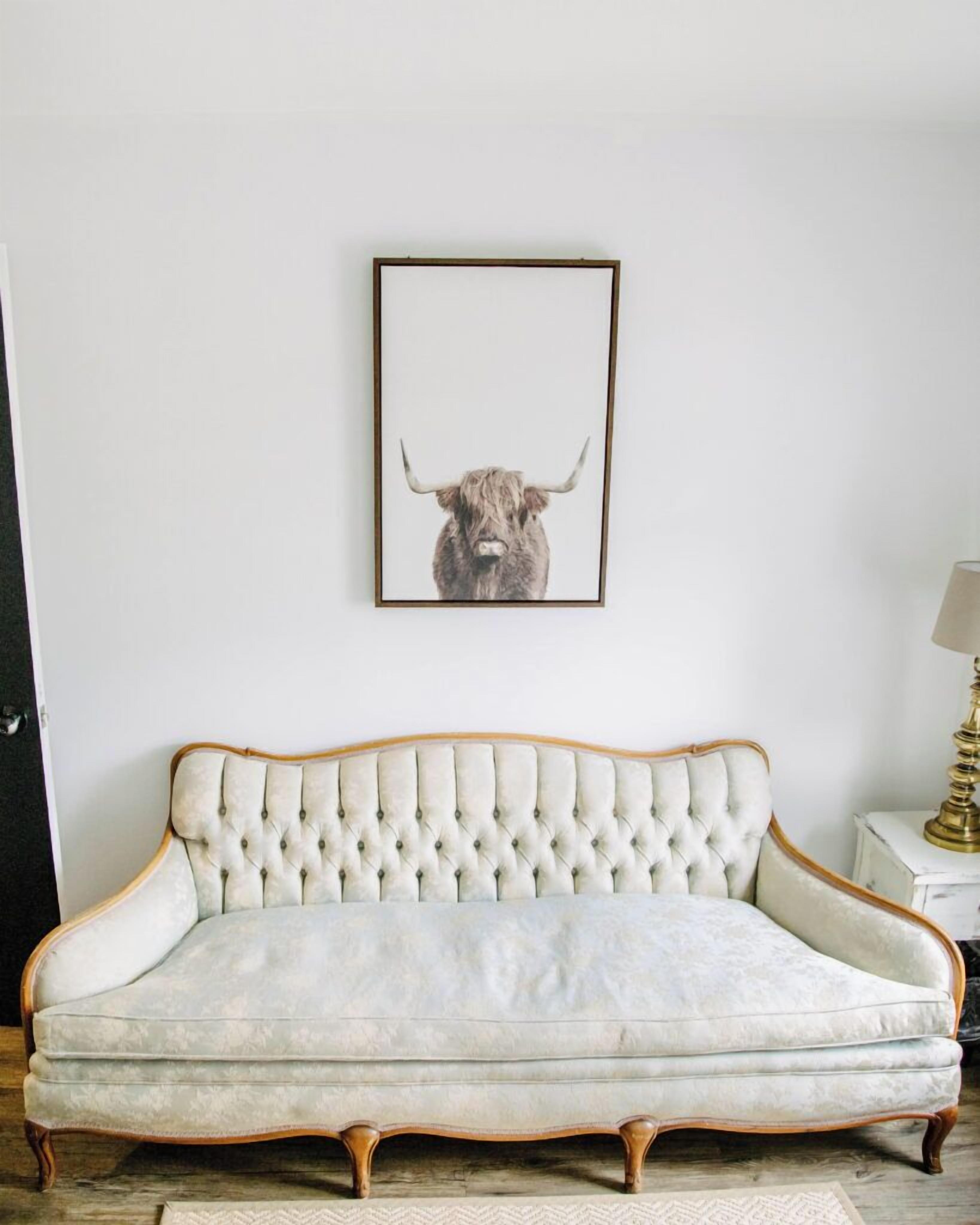 Ein gebürstetes Sofa mit Holzrahmen, ein gerahmtes Kunstwerk mit einem Stierkopf an der Wand und eine Lampe auf einem Beistelltisch.