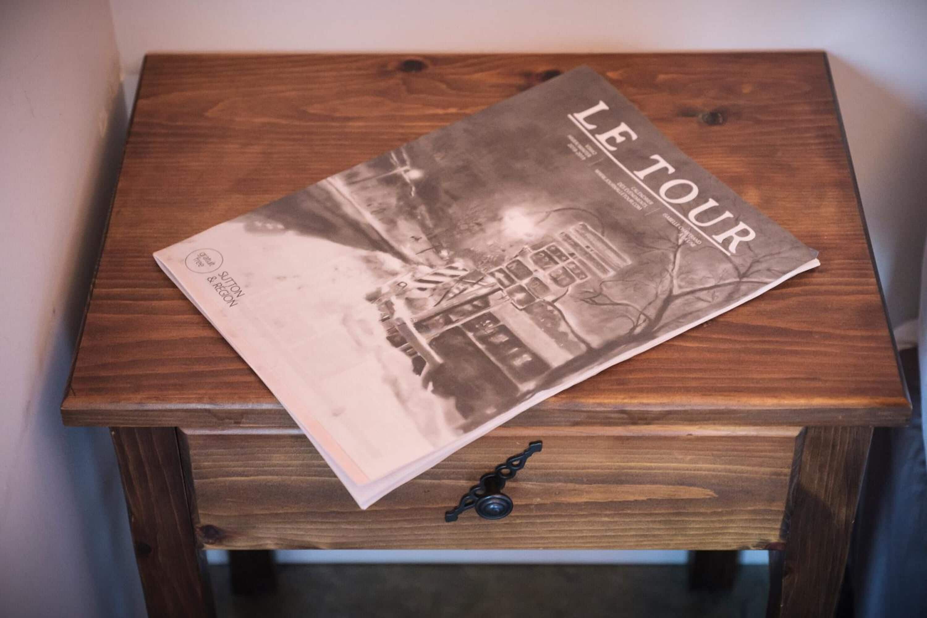 A book titled "LE TOUR" on a wooden table with a drawer below.
