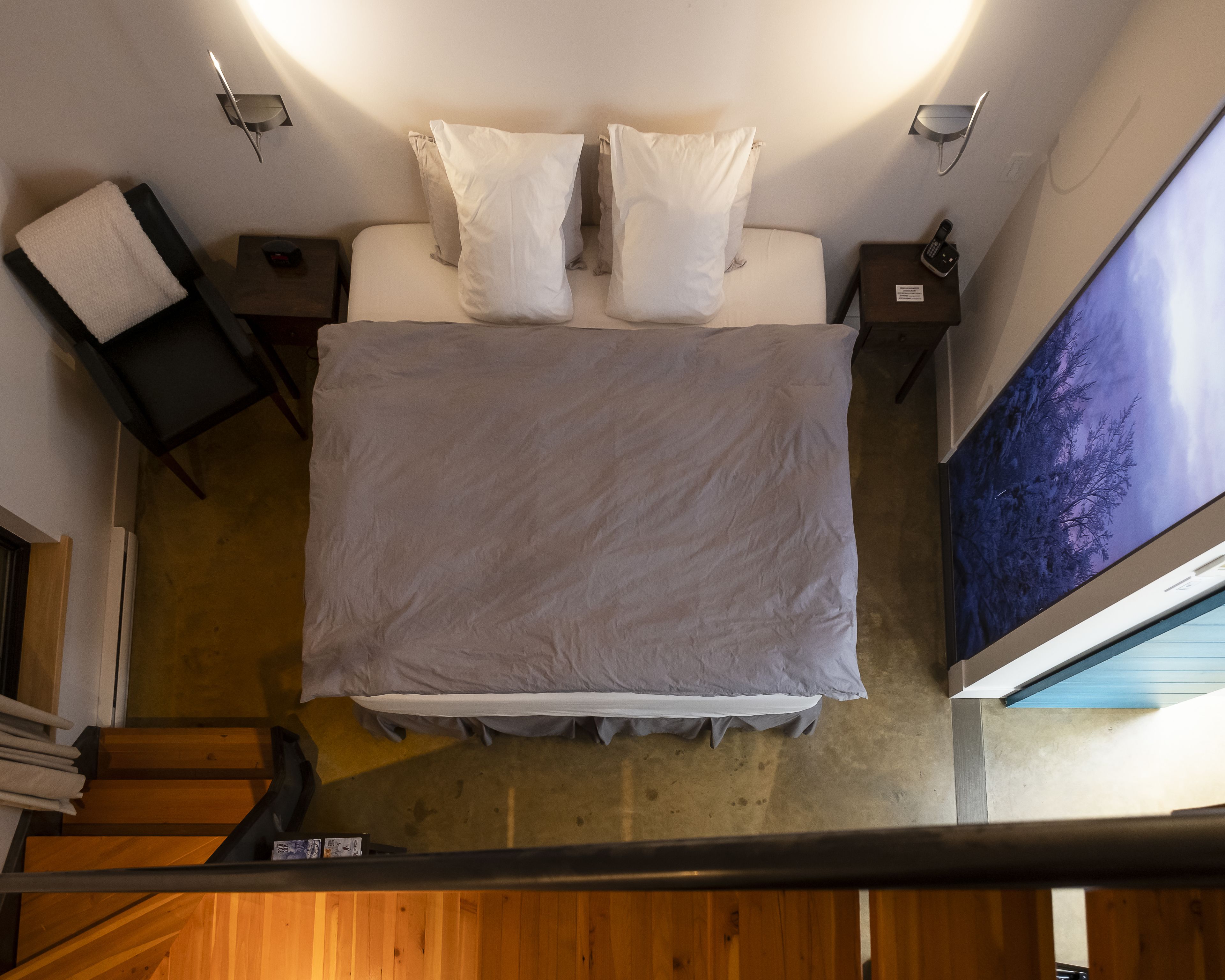 A hotel room with a bed, two bedside tables, a nightstand, a wall-mounted TV, and a wooden staircase.