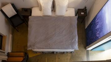 A hotel room with a bed, two bedside tables, a nightstand, a wall-mounted TV, and a wooden staircase.