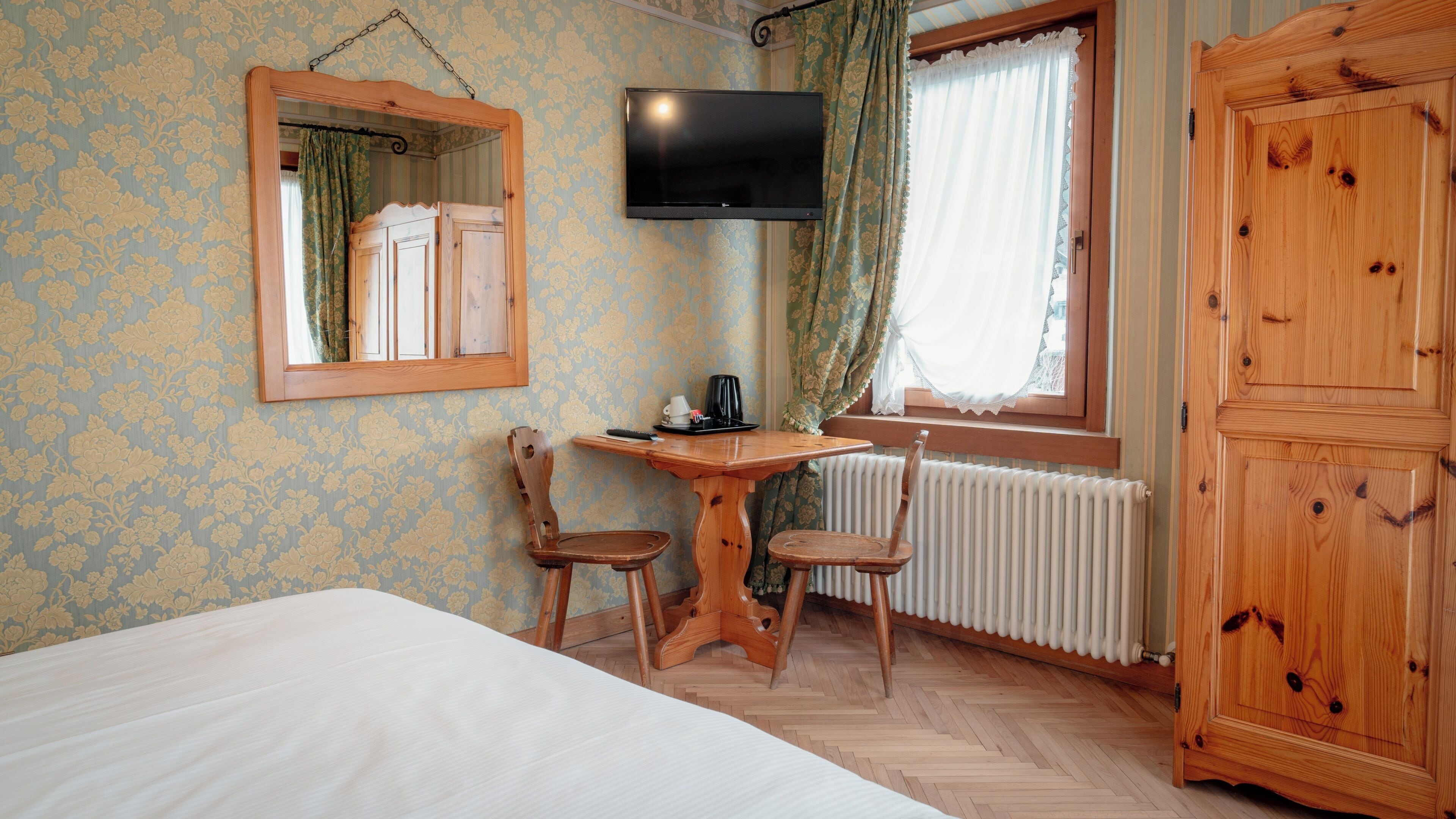 Een slaapkamer met een bed, een houten tafel met stoelen, een televisie, een radiator en een kledingkast.