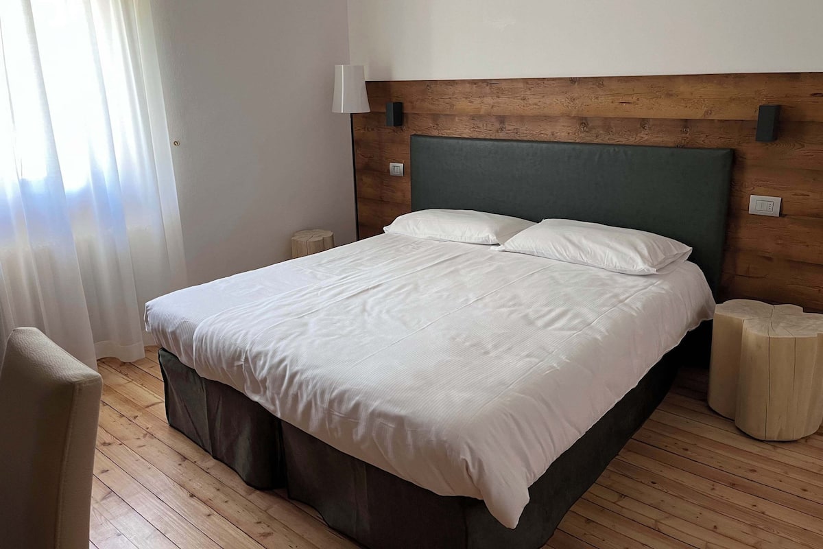 Un llit ben arrenjat en una habitació amb terres de fusta, amb un panell decoratiu de fusta al capçal i una làmpada sobre la tauleta de nit.