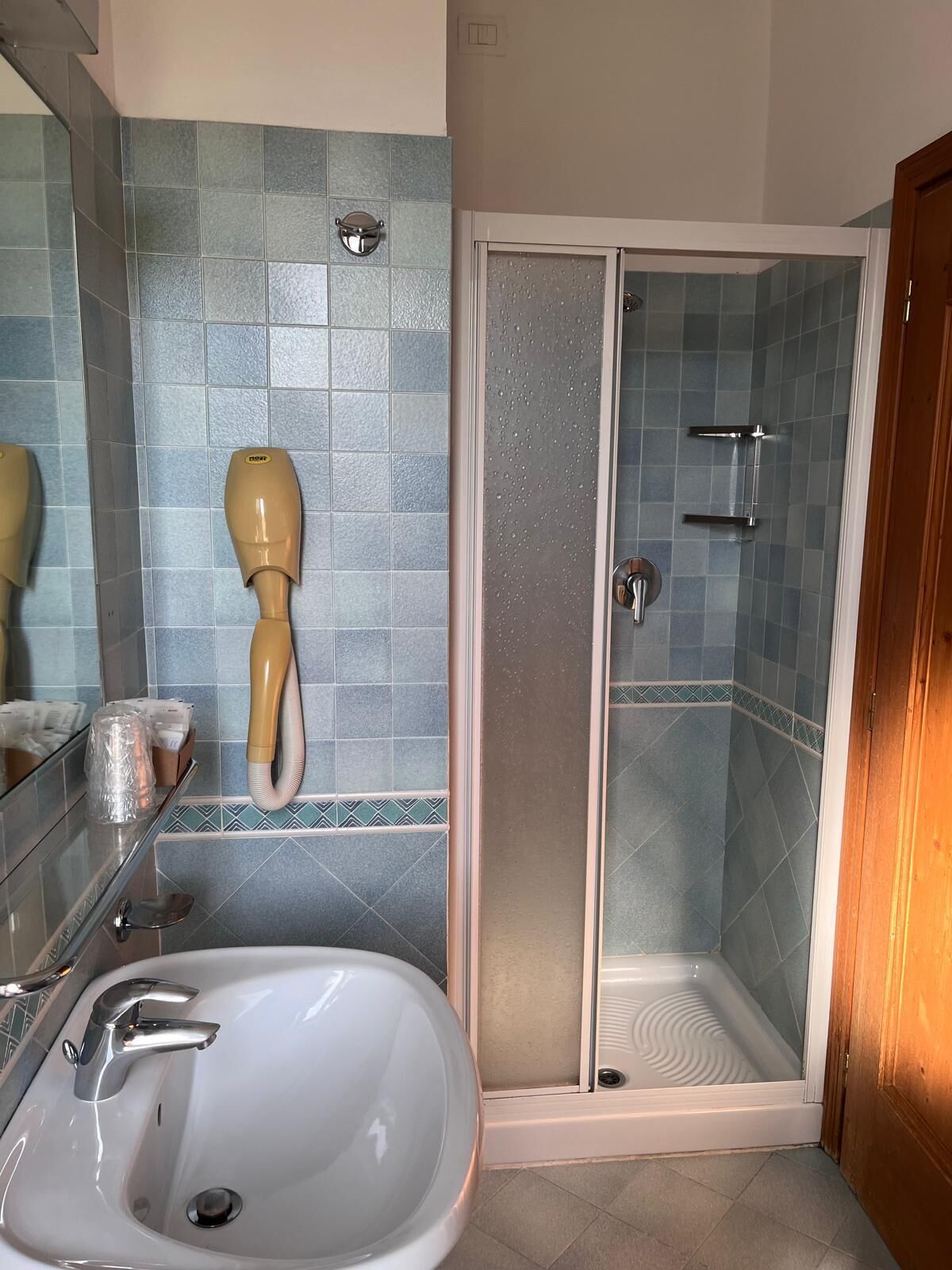 Casa de banho com lavatório, espelho, secador de mãos e cabine de duche com parede de vidro.