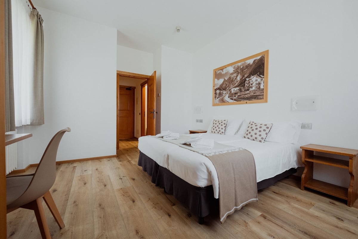 Un dormitori amb un llit, un escriptori i una cadira. Hi ha una porta que condueix a una altra habitació.