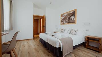 Une chambre à coucher avec un lit, un bureau et une chaise. Une porte donne accès à une autre pièce.