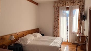 Une chambre à coucher avec une tête de lit en bois, un lit recouvert de draps blancs, une petite table avec une lampe, une chaise et une fenêtre avec des rideaux.