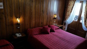 Una habitación con pared de paneles de madera, una cama con ropa de cama roja, dos lámparas fijadas a la pared y un teléfono en una mesita de noche.