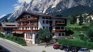 Ein Hotel mit mehreren Balkonen, einer Steinfassade und einer Bergkulisse im Hintergrund.