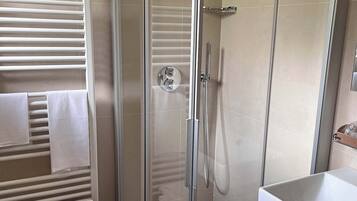Un baño moderno con cabina de ducha de vidrio, un lavamanos blanco y un perchero con toallas.