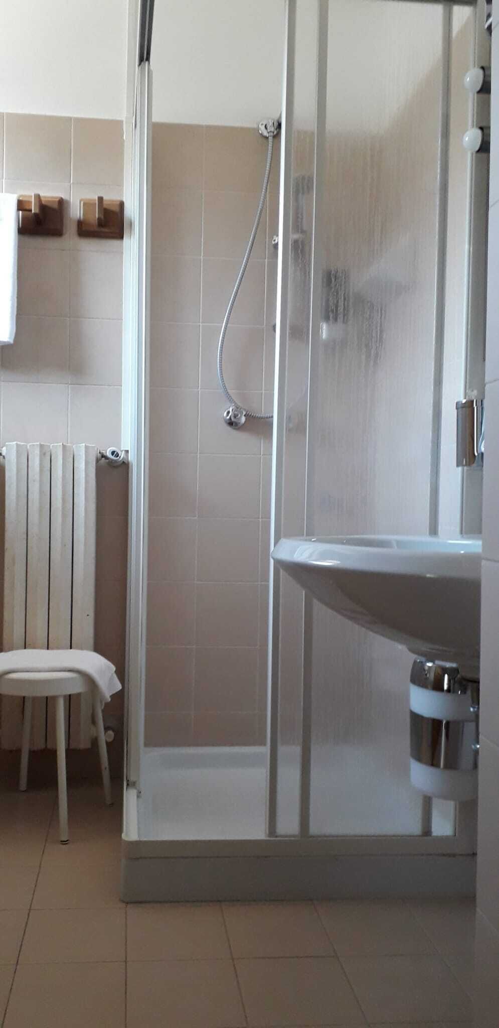 A bathroom with a glass-enclosed shower, a white sink, and a radiator.