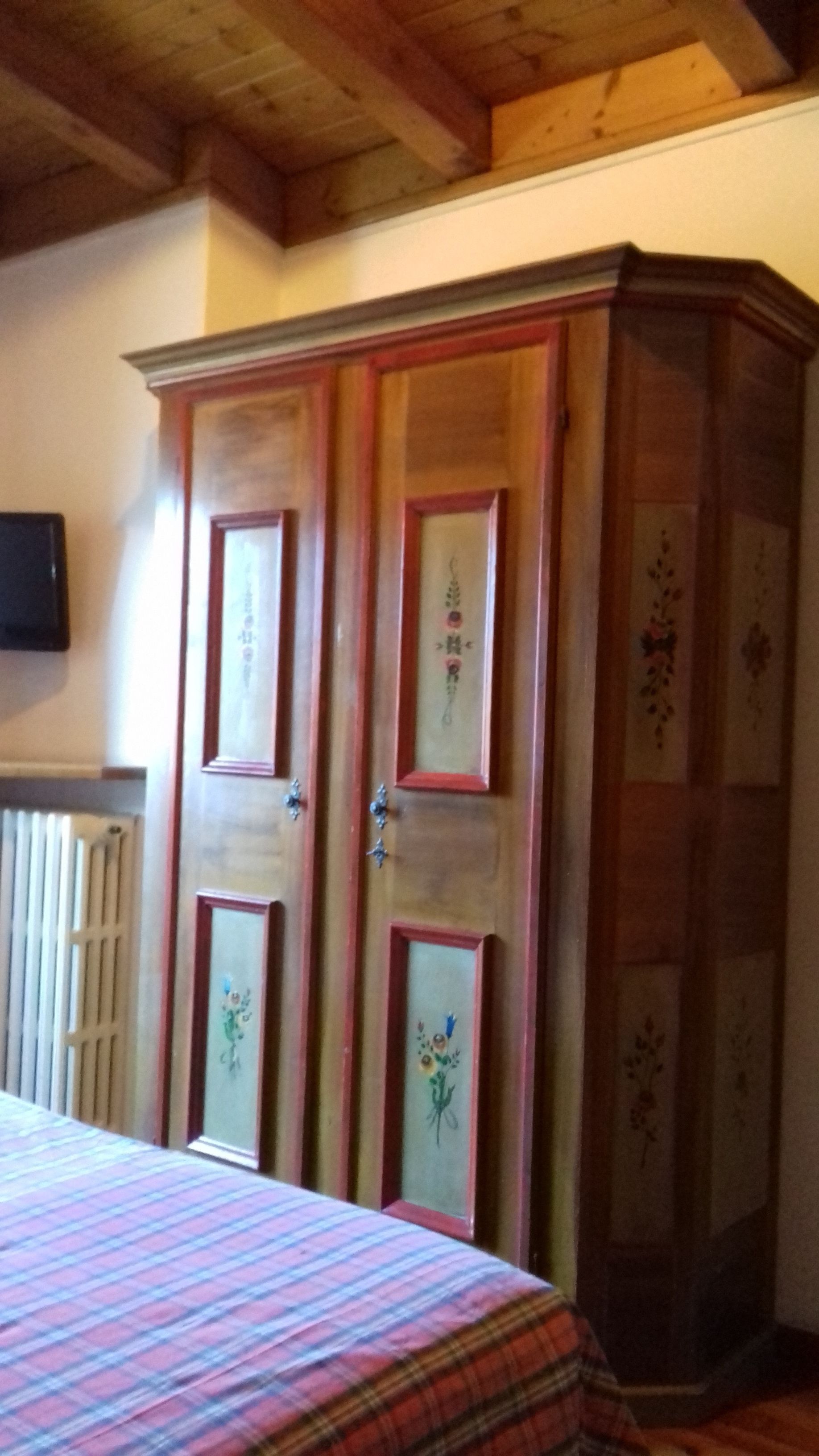 A bedroom with a large wardrobe, a bed with a plaid bedspread, and a radiator on the wall.