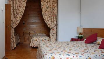 A bedroom with a wooden floor, a bed with floral bedding, a nightstand with a lamp, and a wooden headboard.