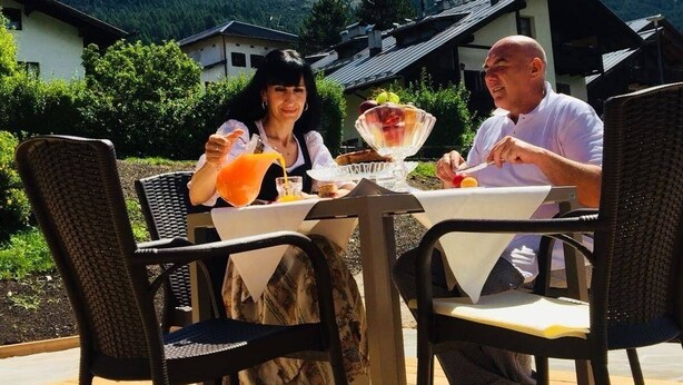 Zwei Personen essen an einem Tisch im Freien mit Blick auf die Berge.