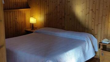 A room with wooden walls, a bed with a white bedspread, a nightstand with a lamp, and a small wooden cabinet.