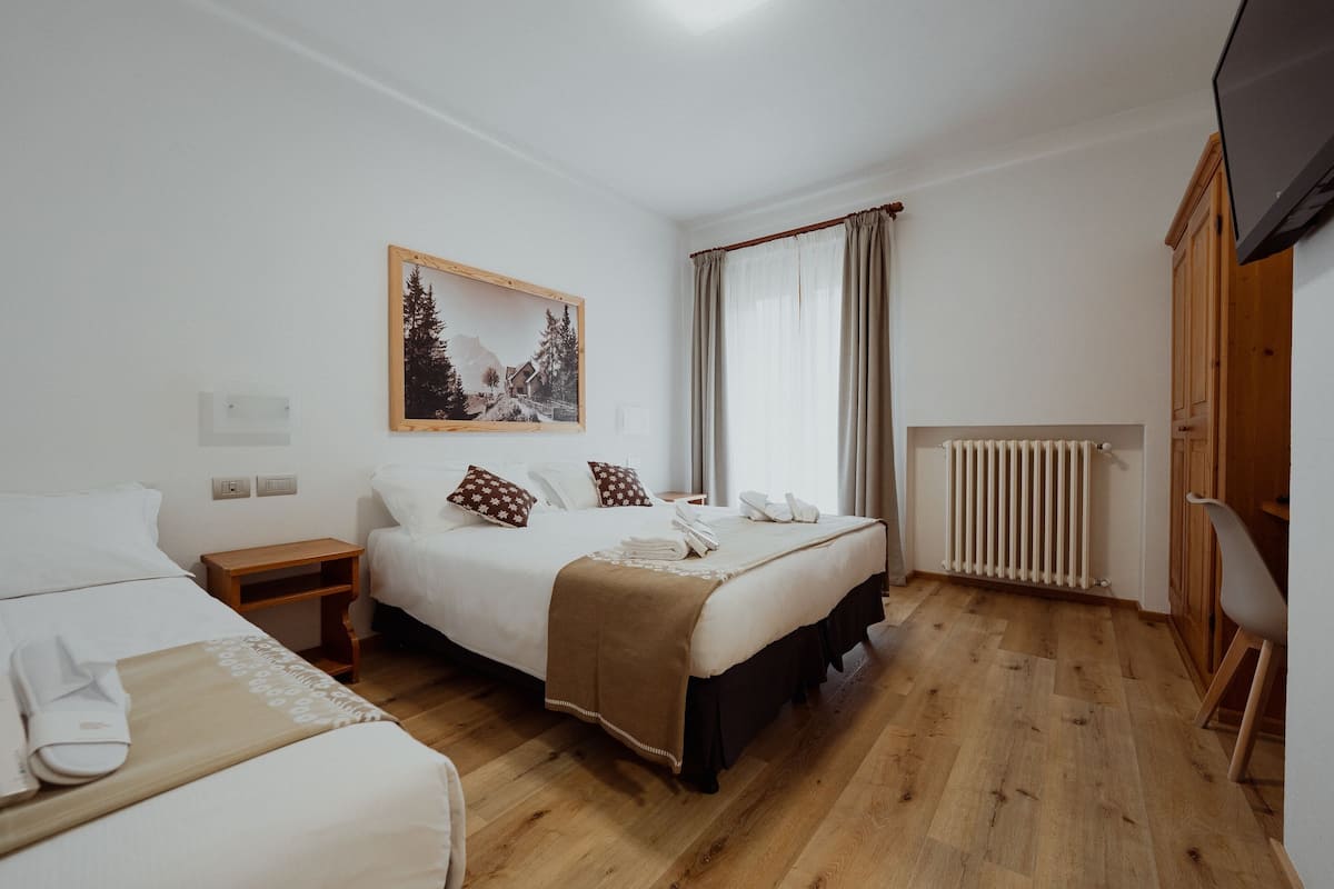 Habitació d'hotel amb dos llits, un sòl de fusta, un quadre a la paret, una finestra amb cortines, un radiador i un televisor fixat a la paret.