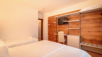 A hotel room with two beds, a desk, a chair, a TV mounted on a wooden wall, and a wardrobe.
