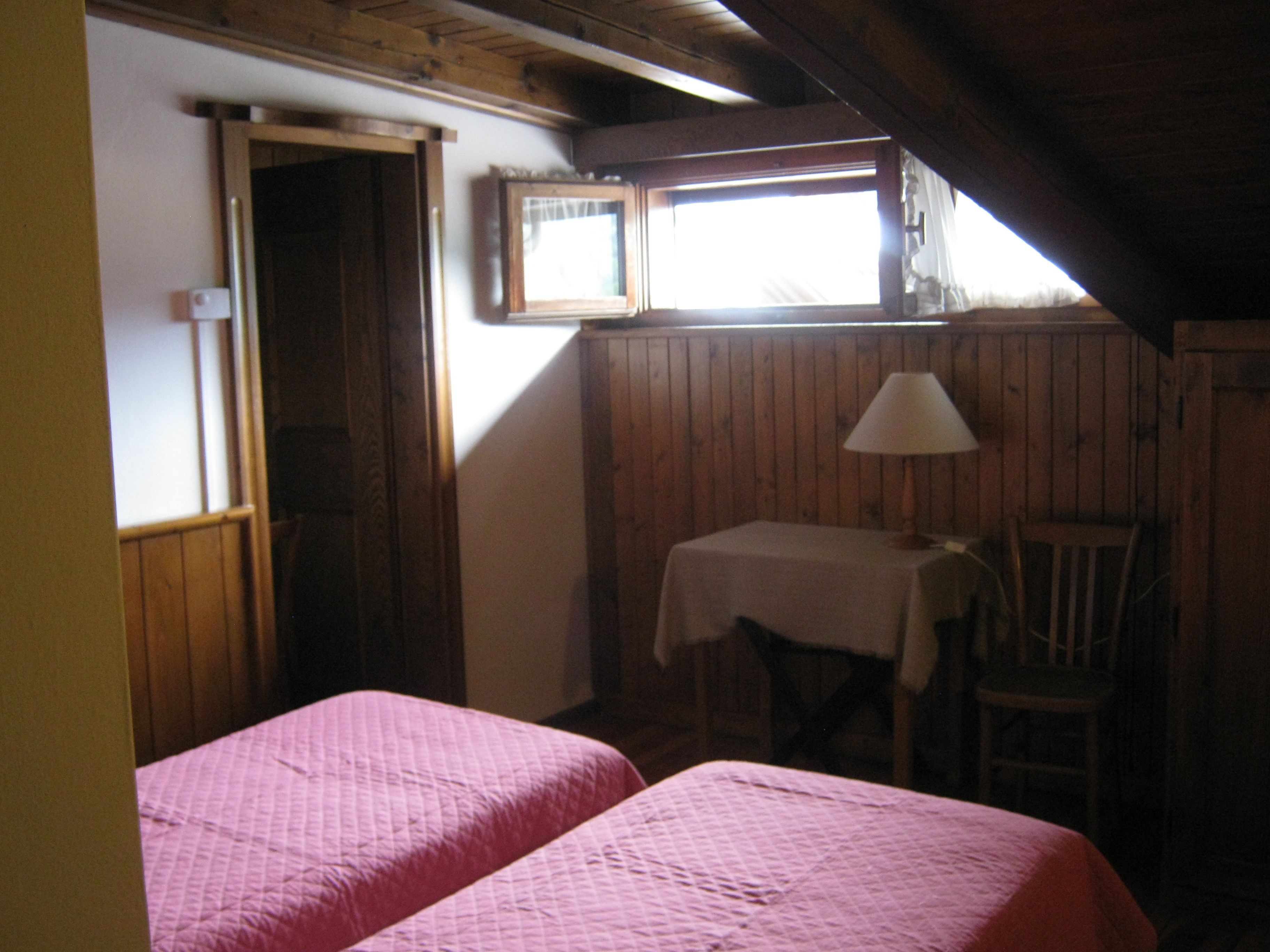 A room with two beds, a table with a lamp, and a window.