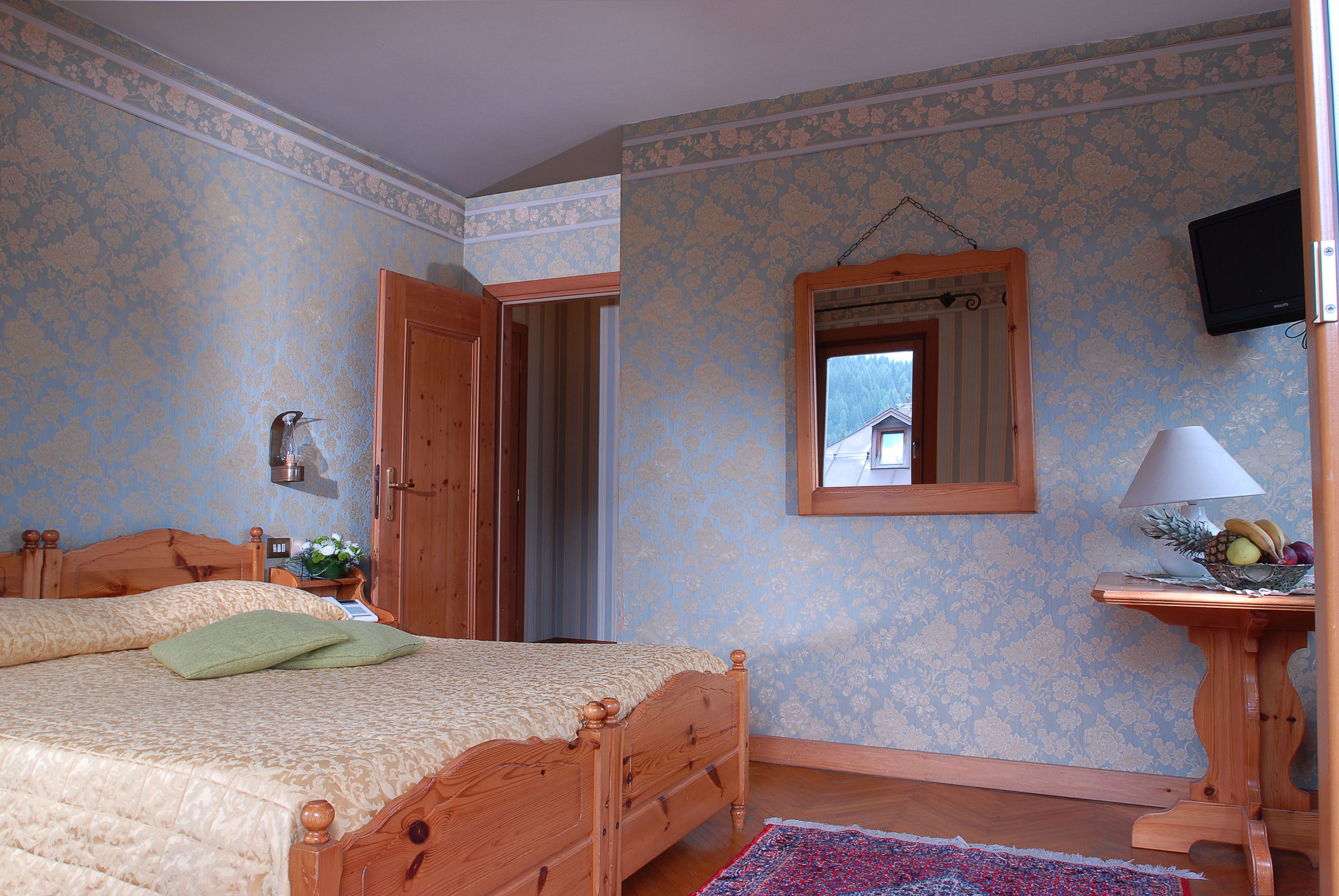 Quarto com cama de madeira, uma mesinha com abajur e televisão na parede.