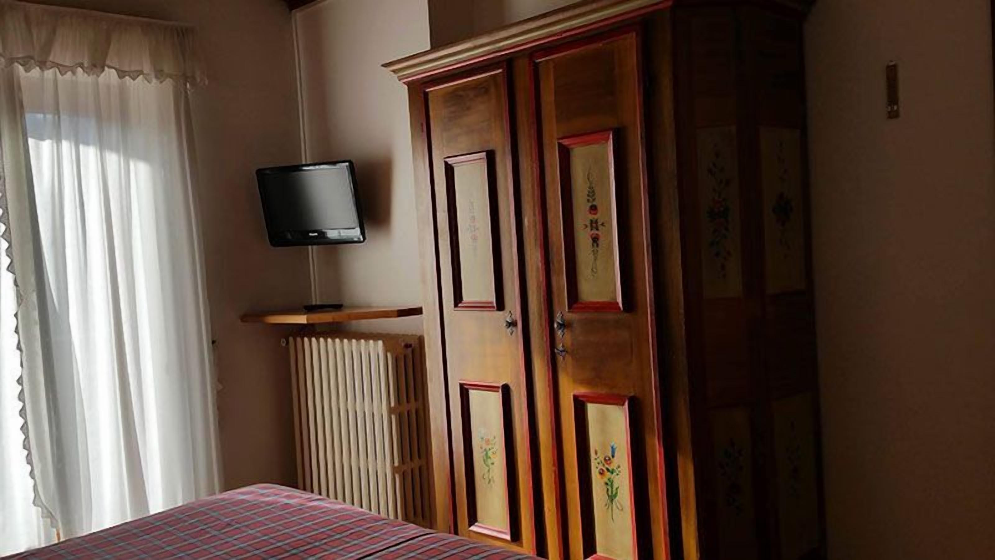 Une chambre à coucher comprenant un lit, un téléviseur posé sur un meuble, un radiateur et une armoire ornée de motifs floraux.
