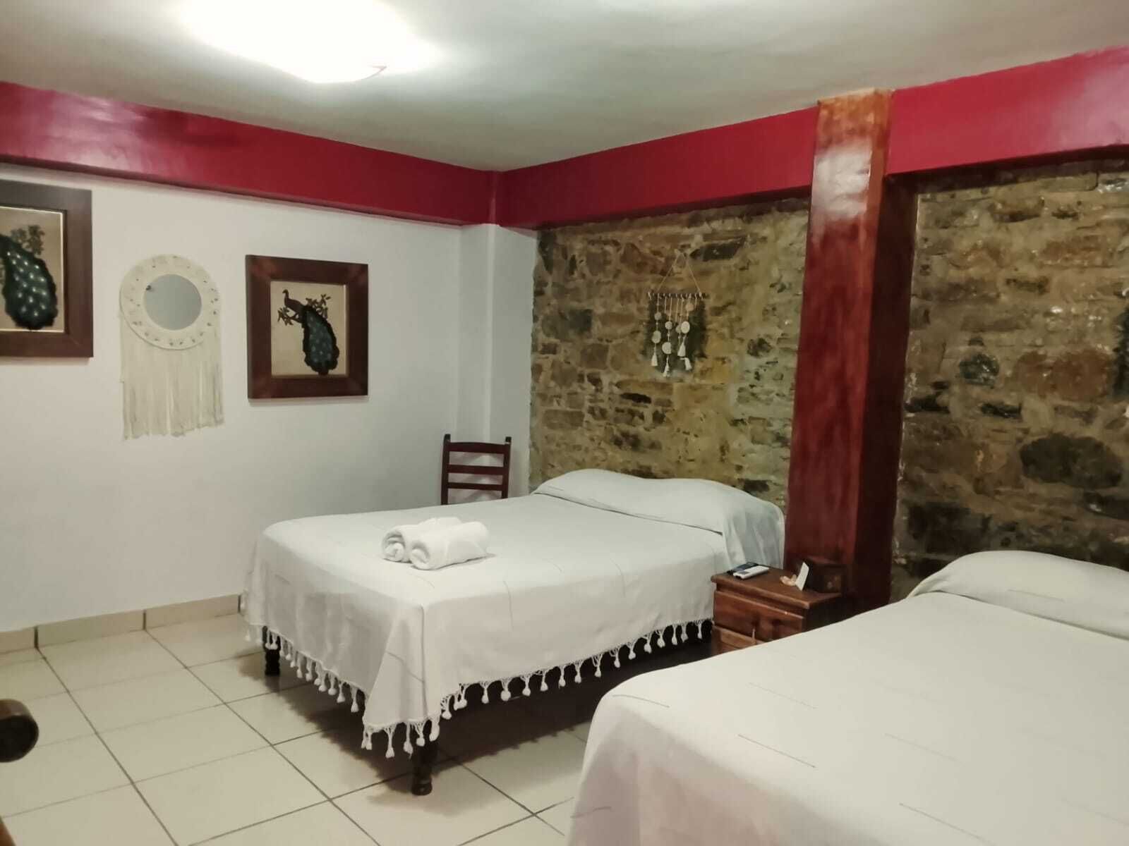 A hotel room with two beds, a stone wall, and a red accent wall.
